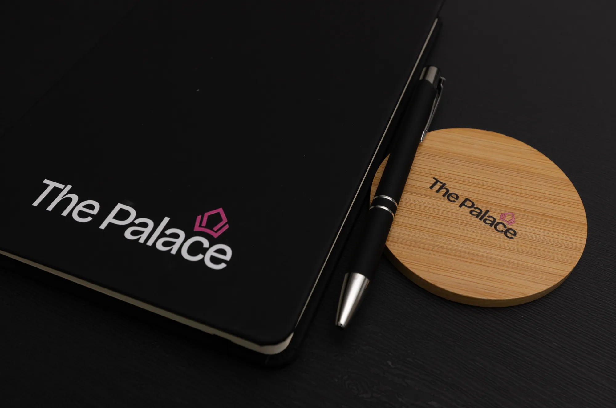 Close-up of The Palace logo on a black notebook and wooden coaster