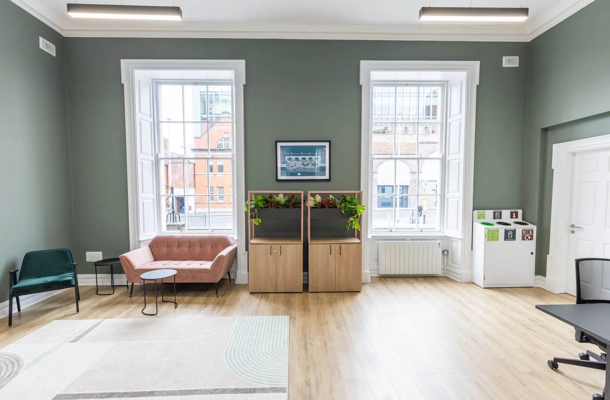 A breakout area with a pink sofa and green armchair between tall windows