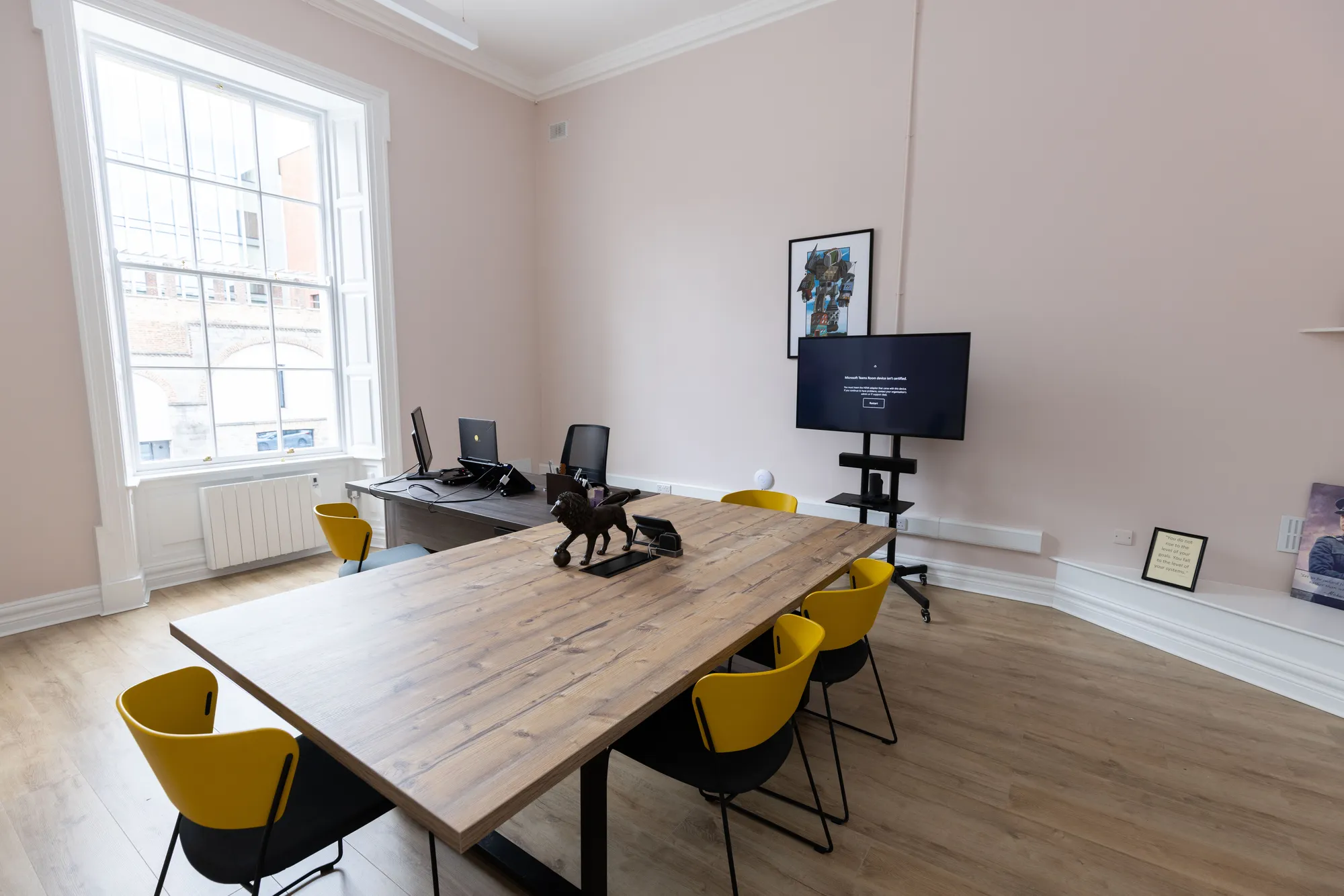 A meeting room with an oak table, yellow chairs and a screen