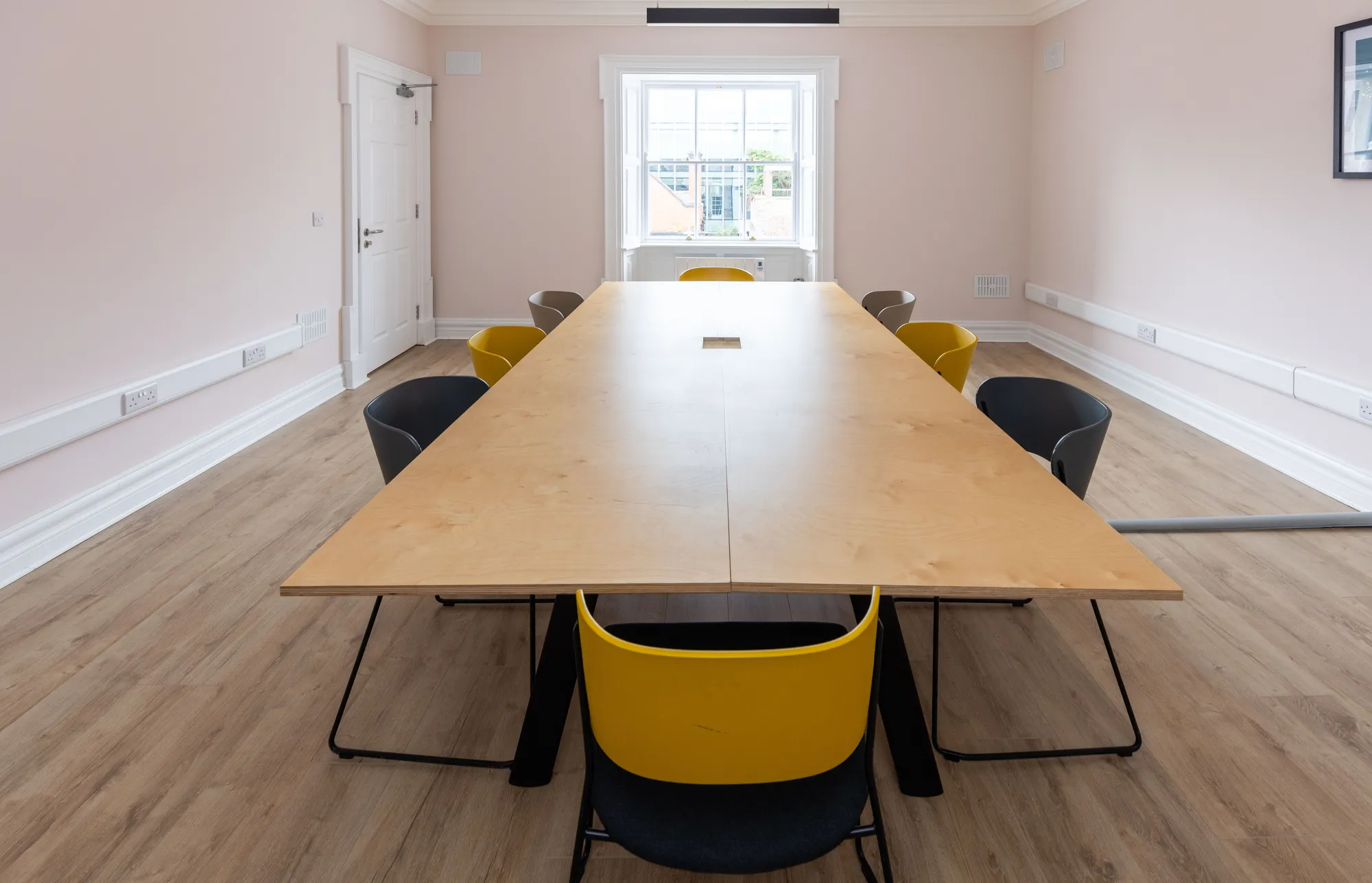 A long oak meeting table with yellow and grey chairs