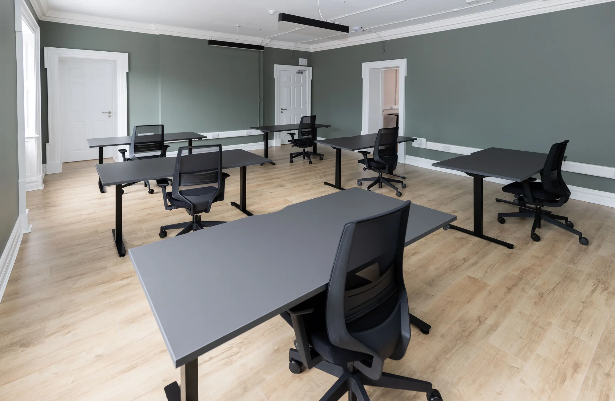 A furnished private office with black desks and sash windows