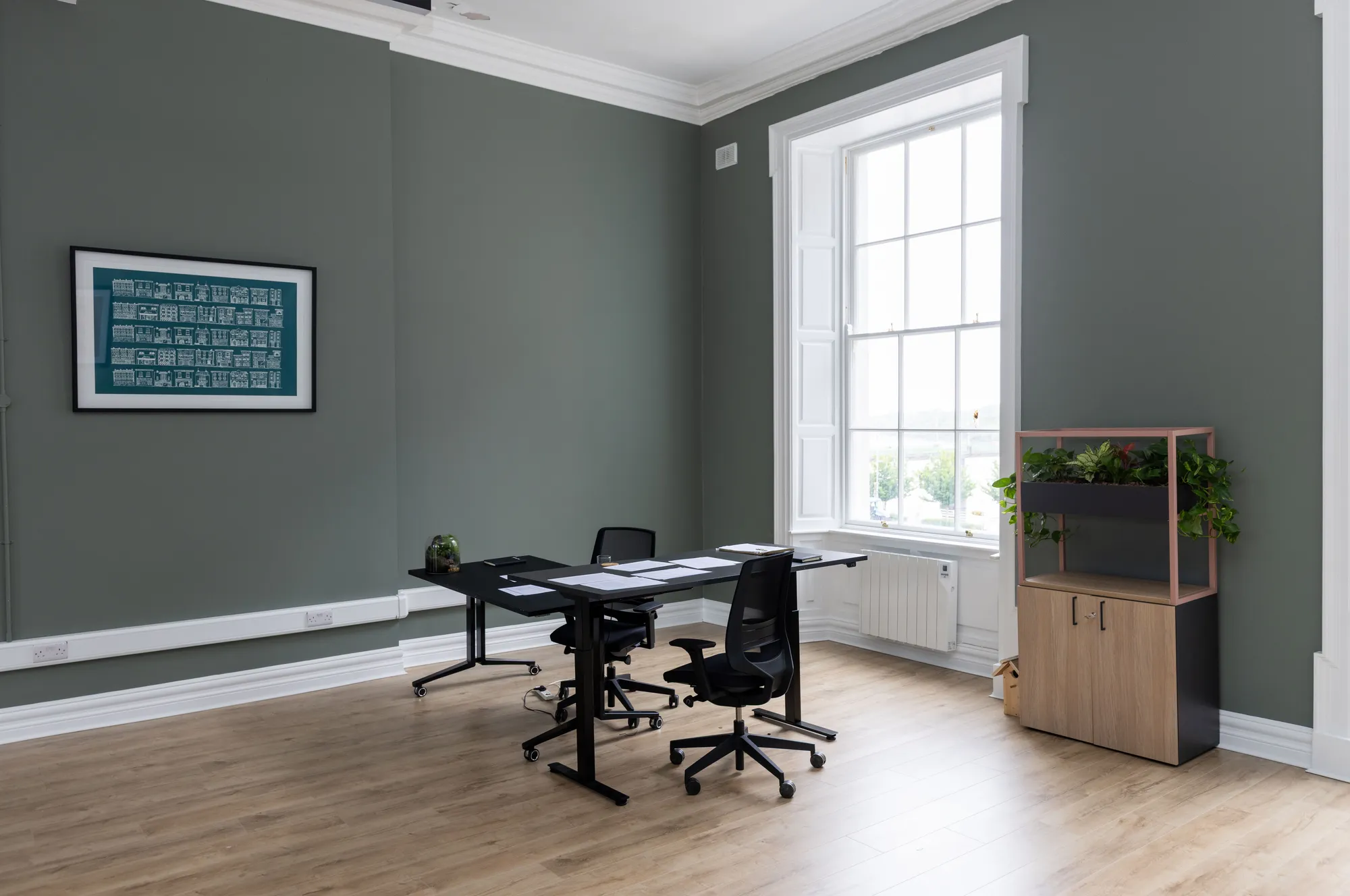 A small private office with a desk, artwork and a planter